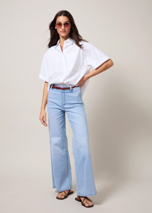 Lysse white oversized short-sleeve shirt styled with light blue wide-leg jeans, a red belt and flat sandals.